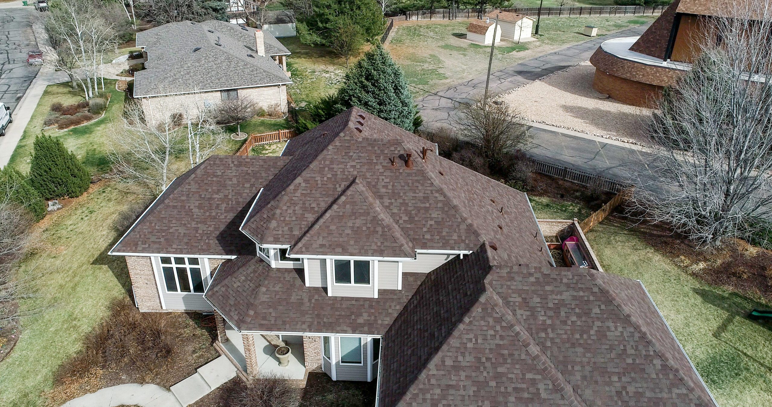 Aerial view of a suburban house with a complex brown shingled roof.